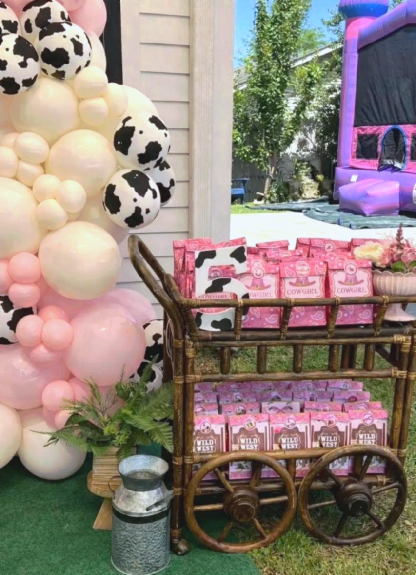 Cowgirl baby shower favor cart with pink gift boxes and balloon arch at Carissa Venue